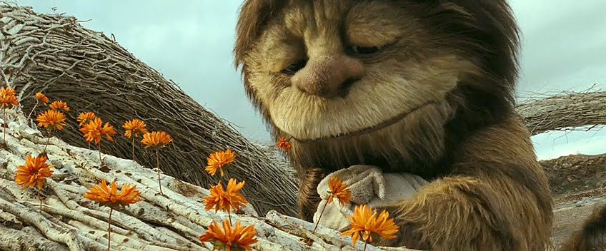 Carol (um monstro peludo e gigante) e Max (um garoto de 10 anos) se abraçam em meio a flores laranjas.